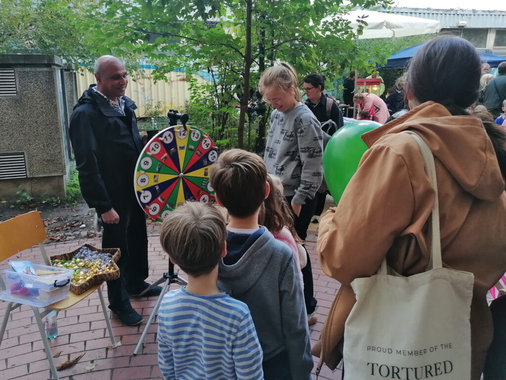 Schlange von Kindern und Erwachsenen am Glücksrad, Süßigkeiten als Preise