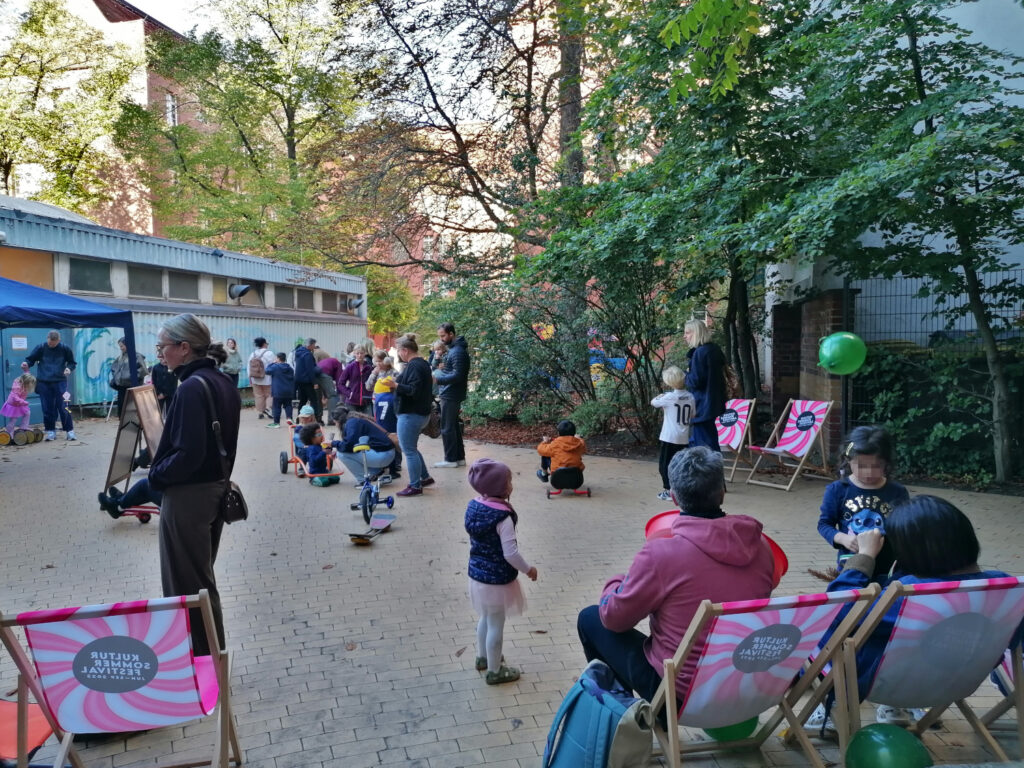 Kinder spielen im Freien, Eltern auf Liegestühlen